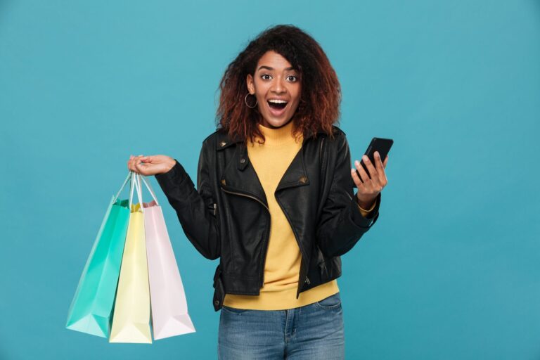 excited african woman holding shopping bags mobile phone